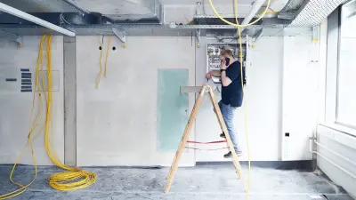 Marco Krause makes a phone call while standing on a ladder at a control cabinet with his smartphone.