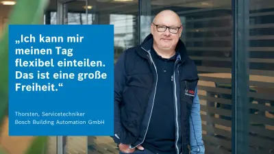 Mitarbeiter lehnt lächelnd an Glaswand