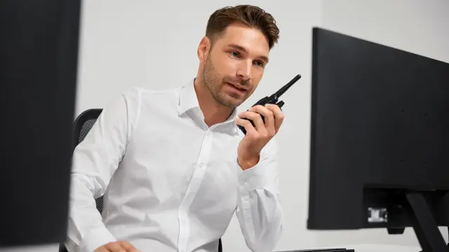 Mann sitzt vor Bildschirm und spricht in ein Funkgerät