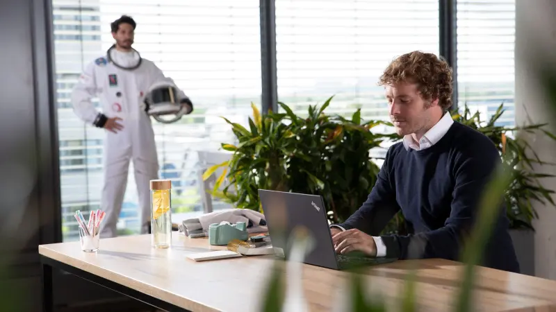 Mann am Laptop, Astronaut im Hintergrund