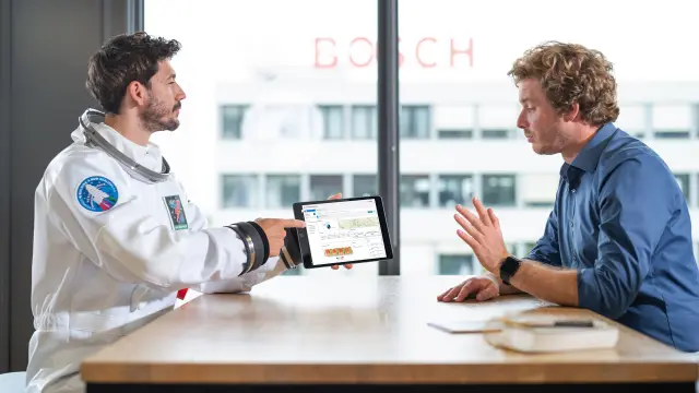 NEXOSPACE Datanaut types on a tablet in a modern office environment, which a man in a blue shirt next to him is holding in his hand.