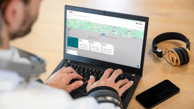 Over the shoulder view of Datanaut sitting at a desk typing on a laptop keyboard, with a smartphone and headphones lying next to the laptop on the table. 