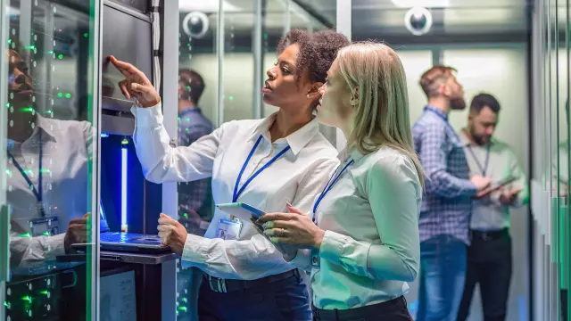 Woman in black blazer smiles while working with tablet in modern office with large windows