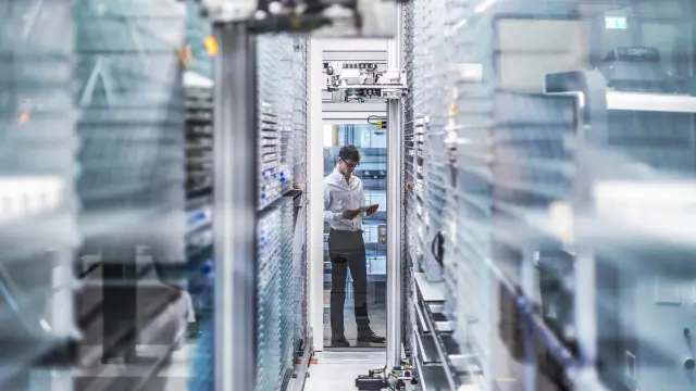 Man in white shirt standing with tablet between server racks in modern data center.