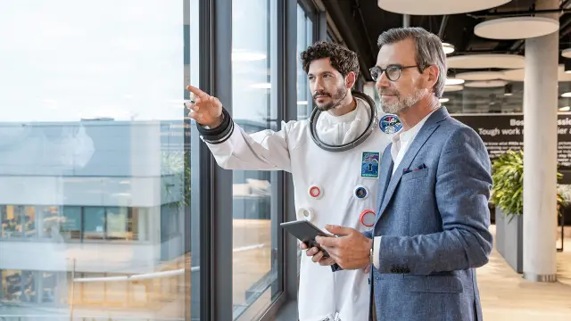 Mann in Anzug und Datanaut stehen am Fenster in modernem Büro und betrachten das Stadtpanorama.