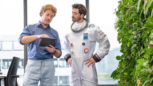 Mann in Hemd zeigt Astronauten Tablet-Inhalte in modernem Büro.