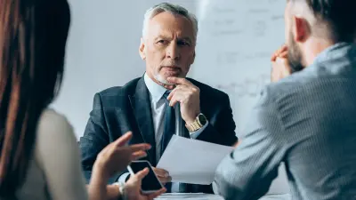 Grauhaariger Bankberater sitzt gegenüber von Mann und Frau im Beratungsgespräch.