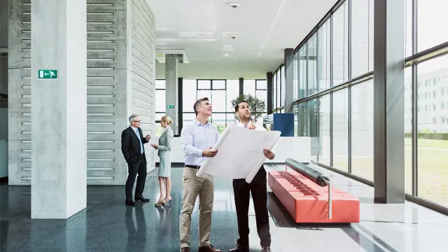 Eingangsbereich eines Gebäudes, zwei Männer besprechen die Installation von Brandmeldern an der Decke