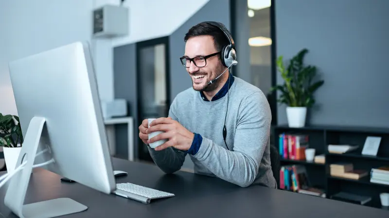 Mann mit Brille und Kaffeetasse sitzt fröhlich vor PC