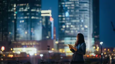 Woman in front of a smart building at night - managed with smart solutions and services from Bosch, GFR and Climatec.