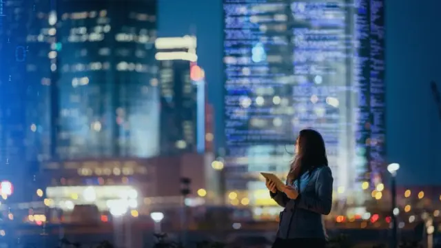 eine Frau steht nachts vor einer Skyline aus smarten Hochhäusern