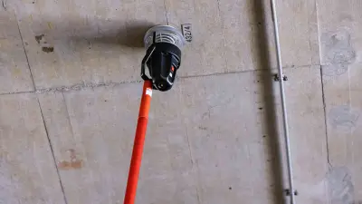 Roland Simion uses a pole to check the fire detector on the ceiling in the snow groomer room.
