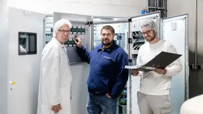 Martin Hartmann and two employees of Allgäu Käse eG in front of the control cabinet
