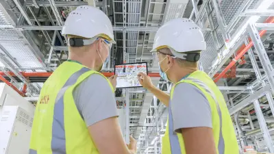 Two employees check the 3D computer model of the chip factory on a tablet using BIM.