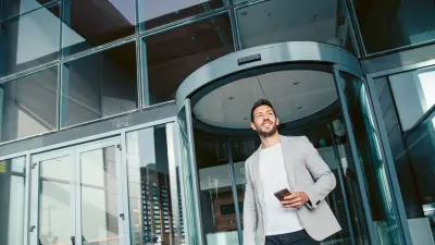 Man exits building through revolving door with mobile phone in hand