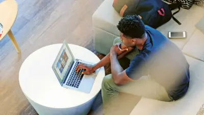 A young man using his laptop while sitting on a couch in an open office space 