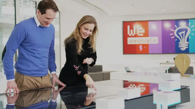 Eine Frau zeigt einem Mann etwas auf einem virtuellen Schreibtisch