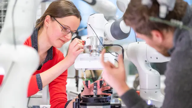 Eine Mitarbeiterin und ein Mitarbeiter schulen einen Roboter, um Objekte im Roboterlabor in Renningen zu erfassen. Mit Hilfe der KI lernt der Roboterarm, Objekte zu erkennen und zu erfassen.