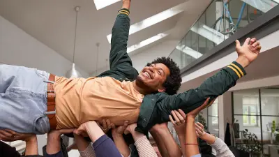 Eine Gruppe von Mitarbeitern trägt einen anderen Mitarbeiter auf den Händen, der gefeiert wird und es genießt.