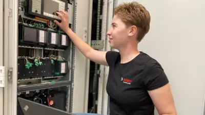 Sabine arbeitet am Schaltschrank, sie sitzt dabei und hat ihren Laptop auf dem Schoß