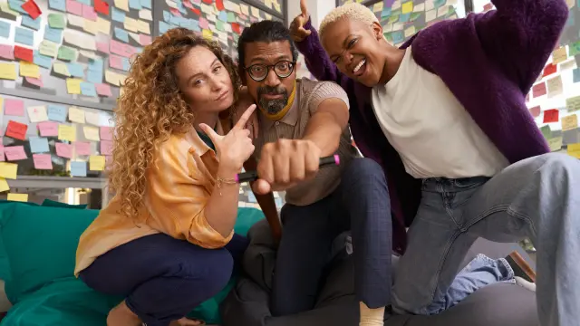 Eine Gruppe von drei diversen Mitarbeitenden mit zwei Frauen und einem Mann schaut in die Kamera und ermutigt dazu, sich zu bewerben bzw. Kontakt aufzunehmen.