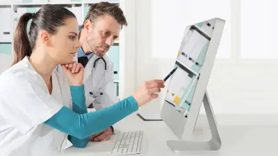 Two healthcare workers are checking data on a monitor