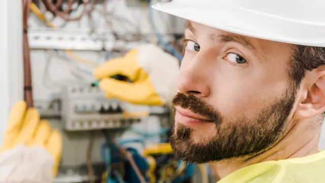 Dos responsables de seguridad de sexo masculino vestidos con chalecos y cascos de seguridad delante de una pizarra y dando una conferencia a una clase. Un hombre sostiene un extintor de incendios