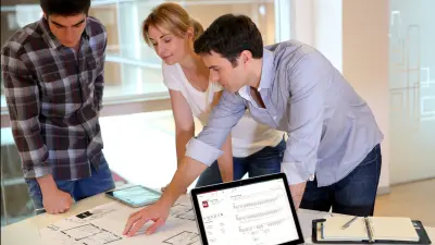 Planners study building plans on a table with a laptop
