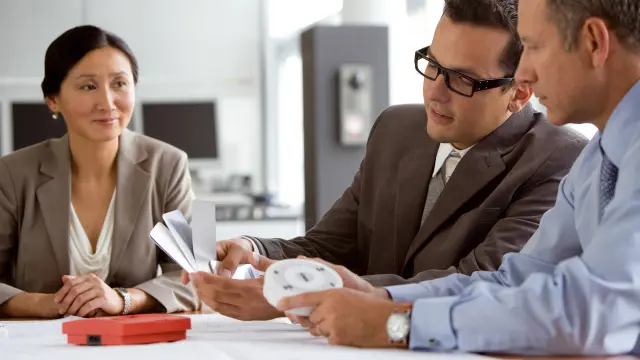 Zwei Männer und eine Frau sehen sich Grundrisse und Bosch Brandmelder an (Handfeuermelder und flacher Melder)