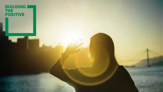 Building the positive: woman looking against the sun in a city by the river
