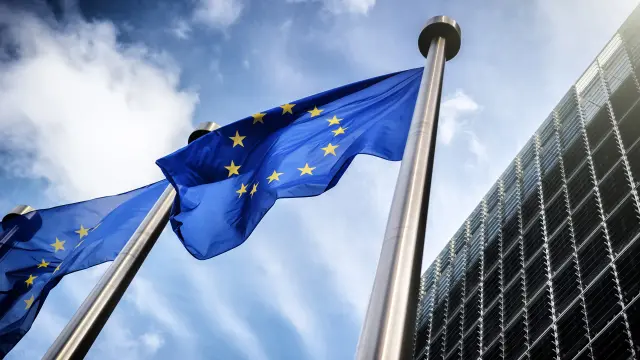 Bandiere europee davanti a un edificio che simboleggia le norme dell'Unione Europea